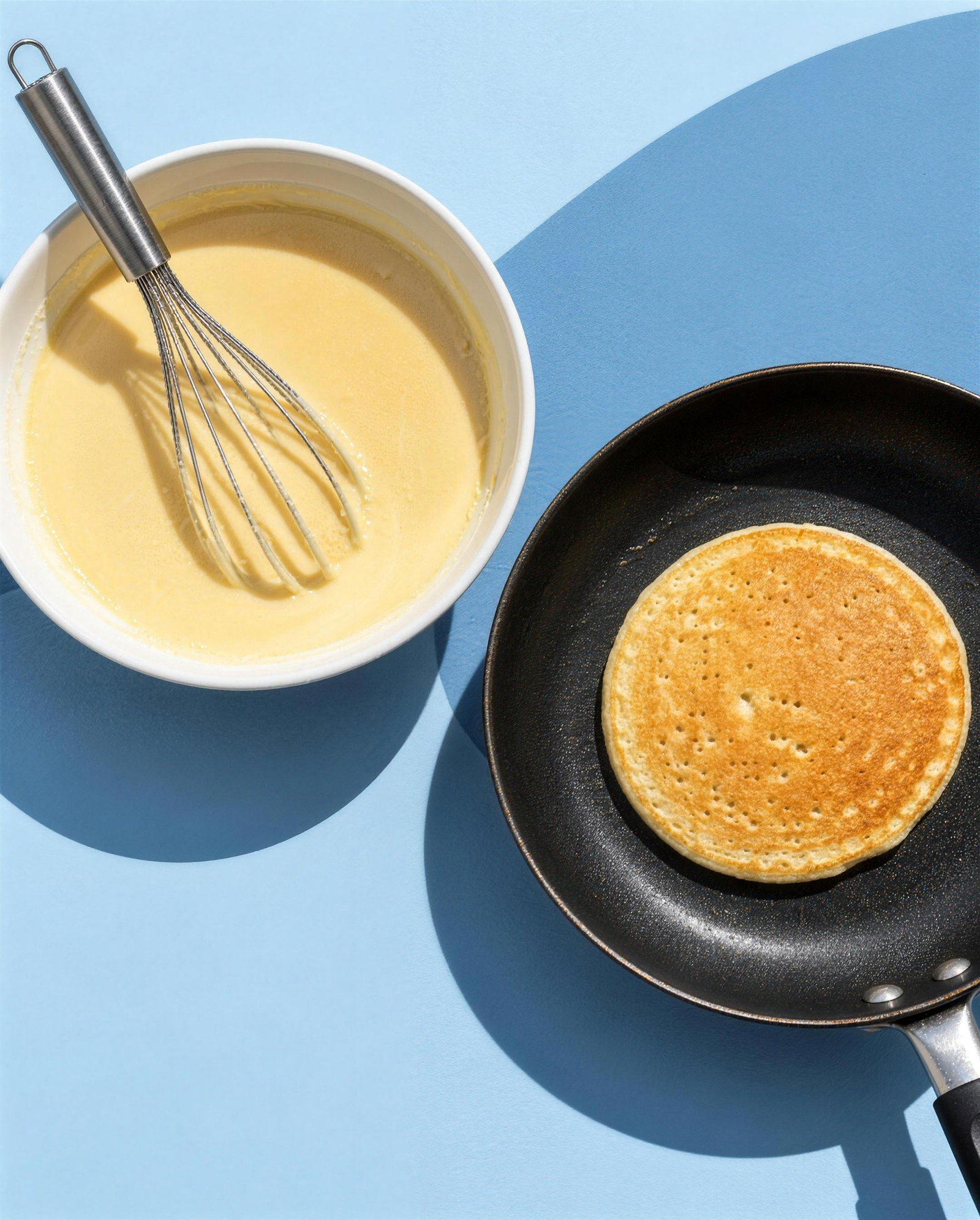 Una ciotola di impasto e un pancake che cuoce in padella